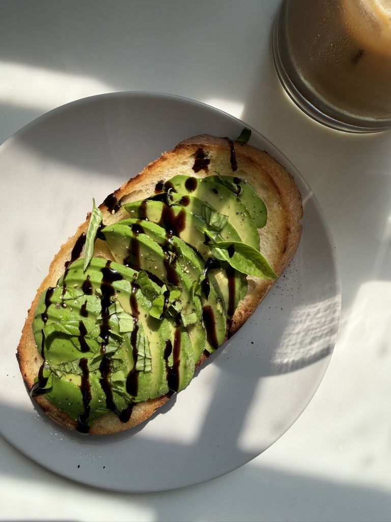 Slice of gluten-free sourdough toast topped with avocado, fresh basil and balsamic